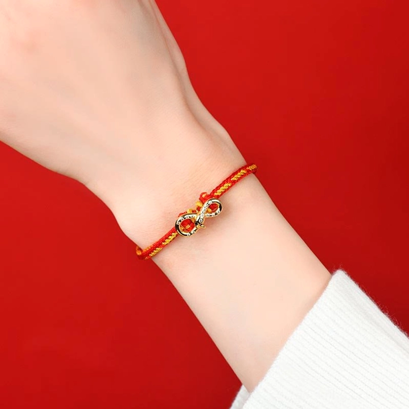 Red String Mobius Snake Year bracelet worn on wrist close-up showing slim red-gold rope and delicate infinity charm against light background