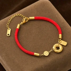 Red string peace buckle fortune bracelet with titanium steel charms and gold hardware on display mat