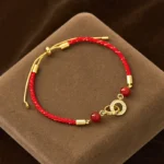 Top view of red string bracelet with gold peace buckle on brown velvet mat