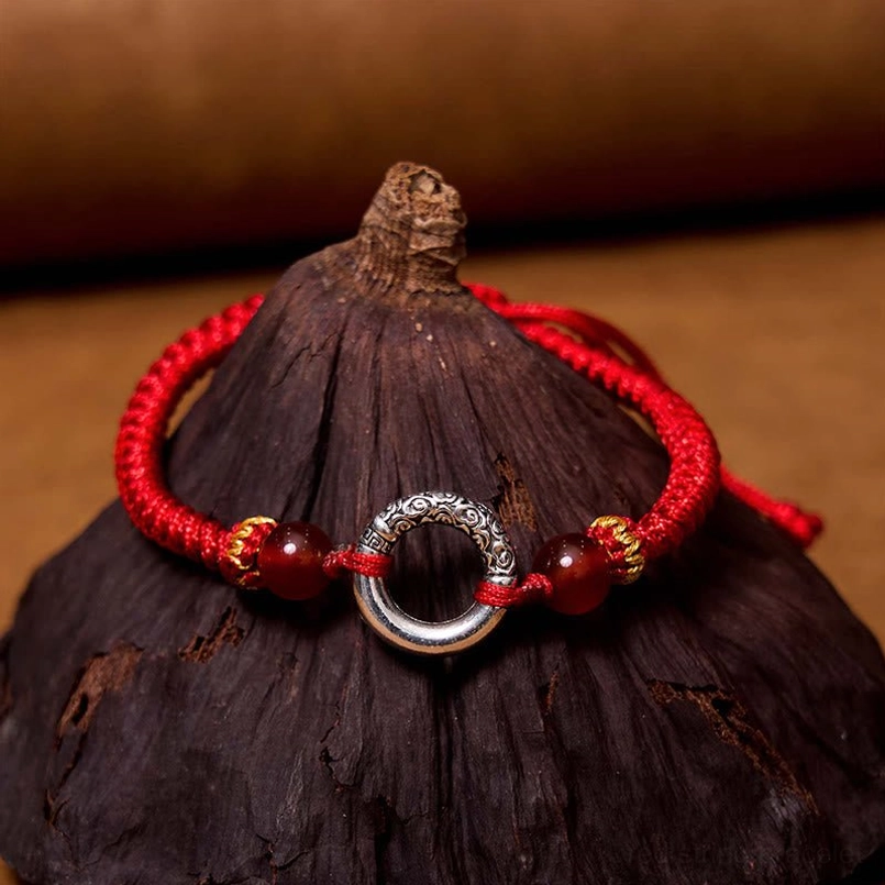 Red braided peace buckle bracelet with silver agate beads and adjustable cord on dark wooden surface