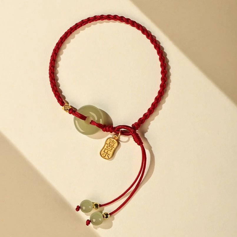 Red braided string peace buckle jade bracelet flat lay close-up with gold charm details