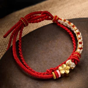 Red string peach blossom double layer bracelet with gold flower charm on wooden background