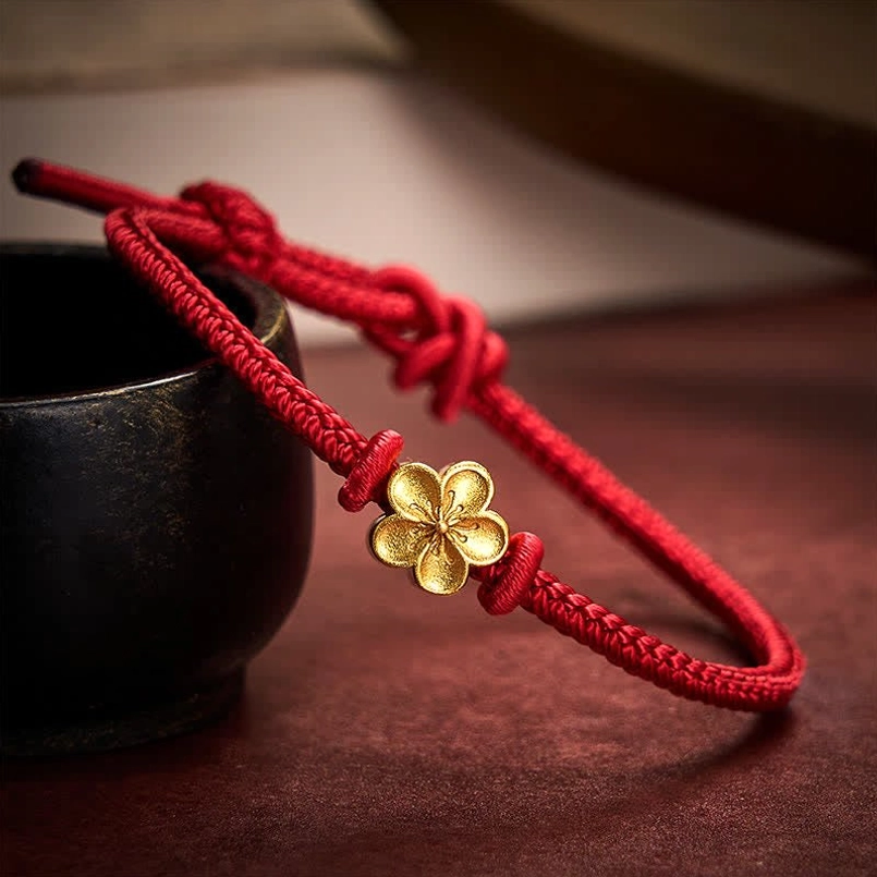 Paired red string peach blossom luck bracelets with gold flower charms on dark surface