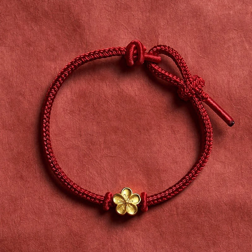 Adjustable red string bracelet with gold flower charm flat lay top view