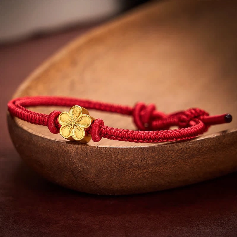Handwoven red string bracelet with peach blossom gold charm on wooden surface