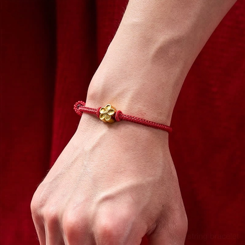 Red string peach blossom bracelet worn on wrist with gold flower charm visible