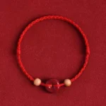 Red string peach wood cinnabar peace buckle bracelet with woven cord detail on dark background