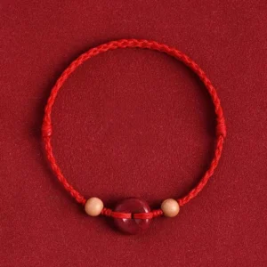 Red string peach wood cinnabar peace buckle bracelet with woven cord detail on dark background