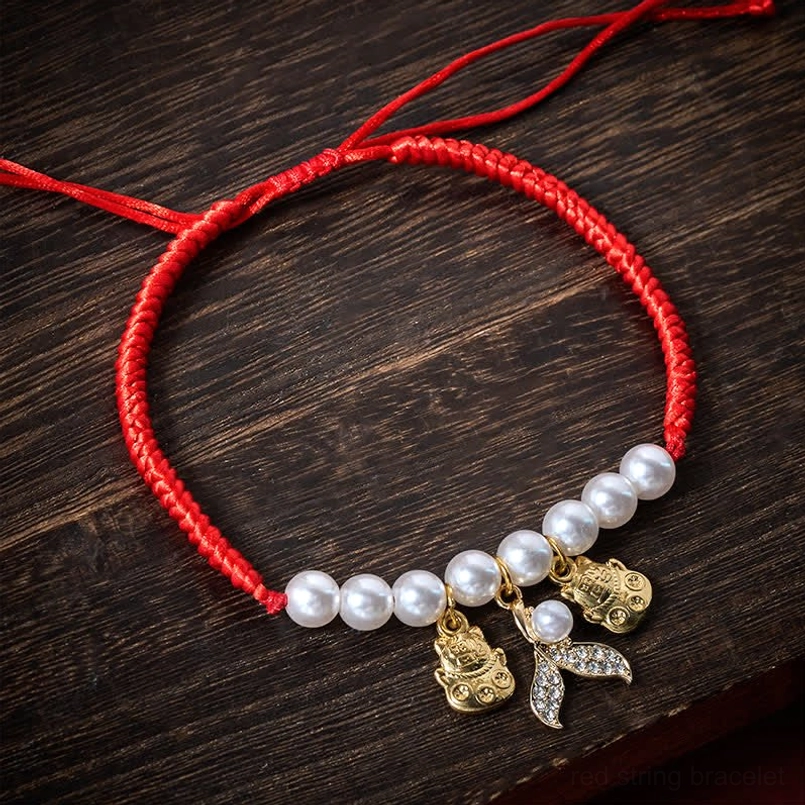 Adjustable red braided pet collar with white pearls and gold lucky cat fish tail charms flat lay top view