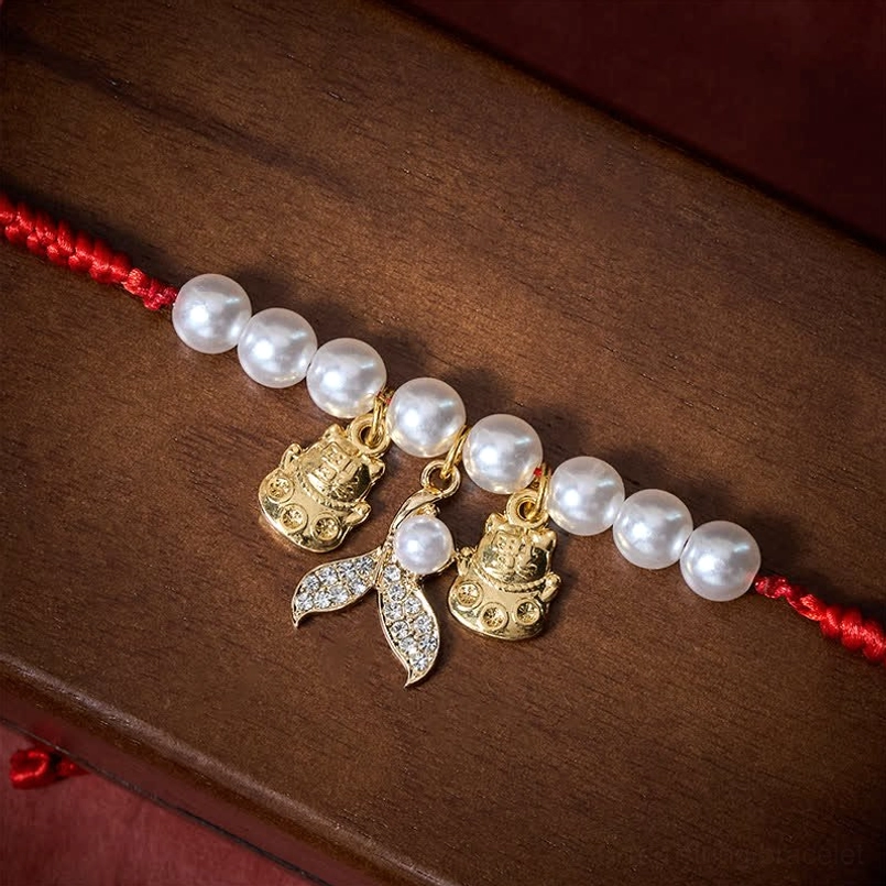 Red braided cord pet collar with white pearls and gold lucky cat fish tail pendants wood surface display