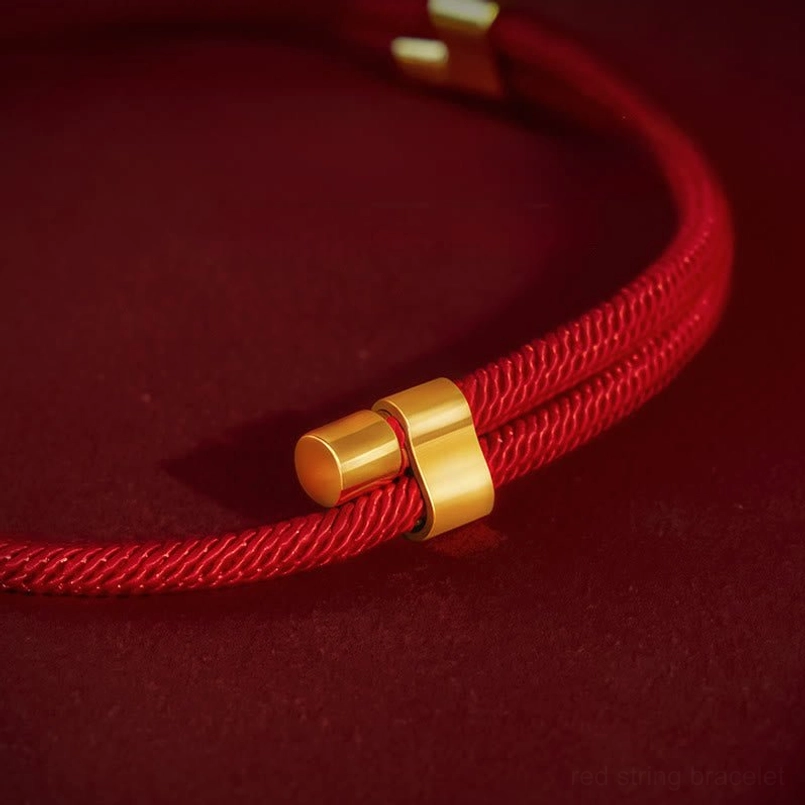 Close-up detail of red string pet collar adjustment mechanism with gold cylindrical clasp