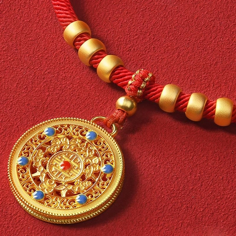 Close-up intricate carved gold compass disc with blue enamel accents on red string rope