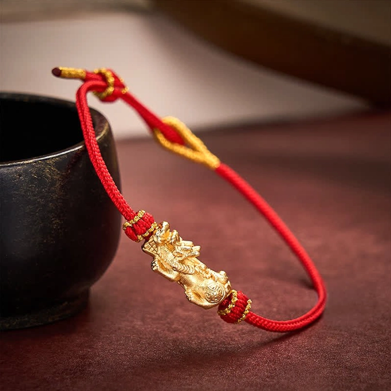 Golden Pixiu charm with red woven cord bracelet on dark wooden table background