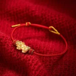 Red string Pixiu luck bracelet with golden charm displayed on red knitted fabric - high angle view