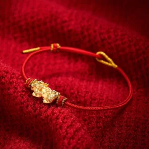 Red string Pixiu luck bracelet with golden charm displayed on red knitted fabric - high angle view