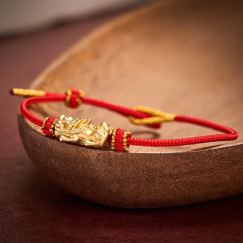 Hand-woven red cord Pixiu bracelet on wooden bowl setting - warm tone lifestyle shot