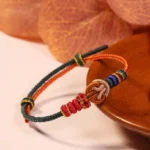 Red hand-woven prosperity knot bracelet with decorative beads displayed on wooden plate