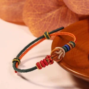 Red hand-woven prosperity knot bracelet with decorative beads displayed on wooden plate