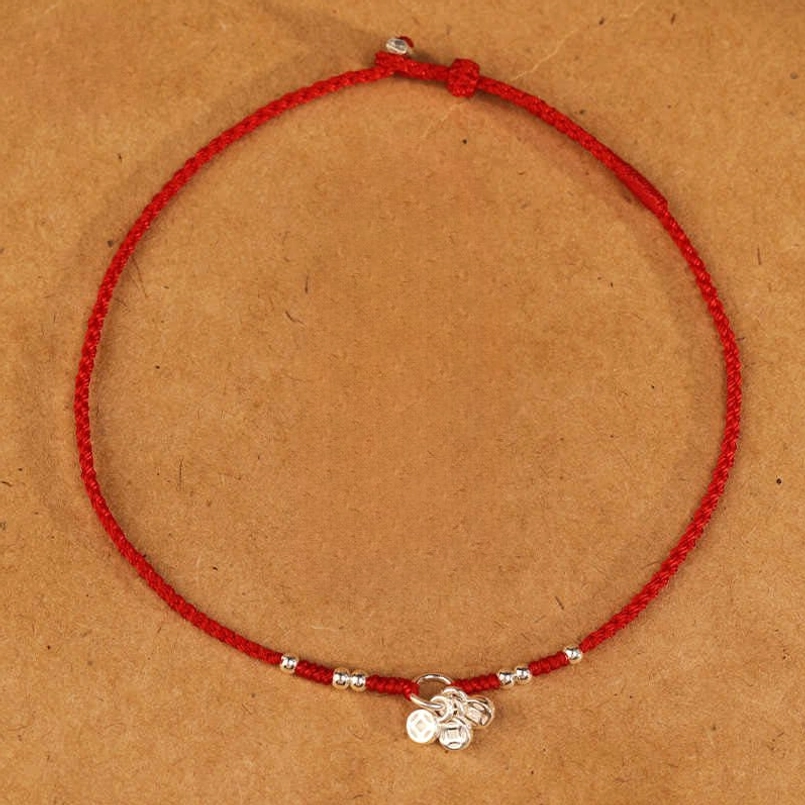 Red string protection bracelet flat lay tabletop display with silver beads and coin charm