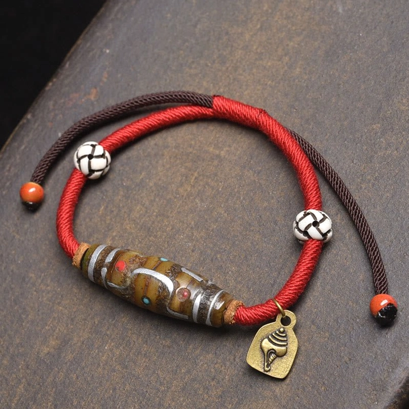 Red string protection bracelet flat lay with red brown cords patterned beads and metal conch charm