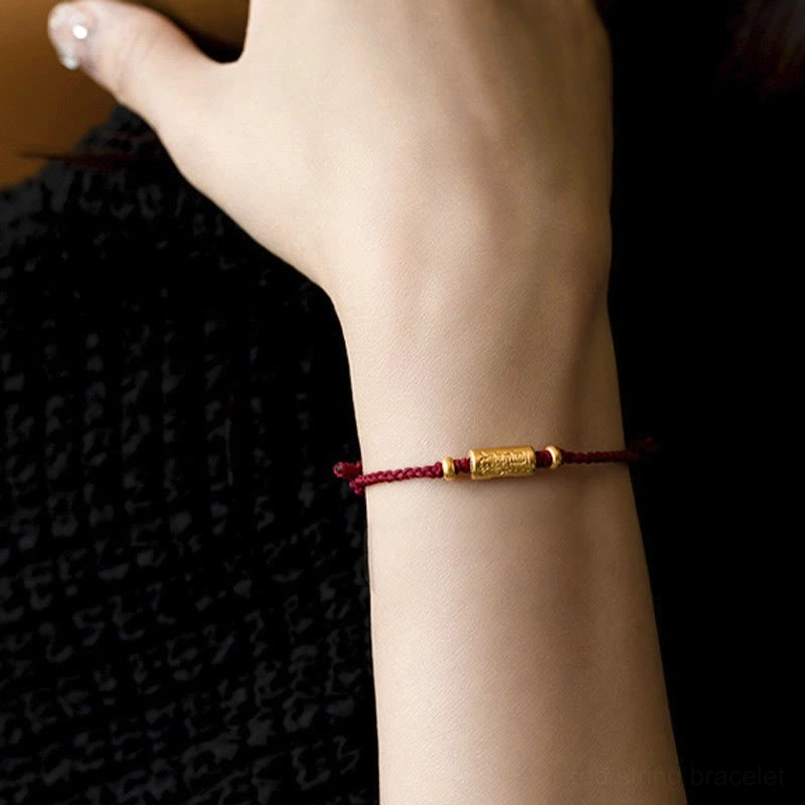 Red lucky bracelet with carved gold charm on wrist - close-up side view