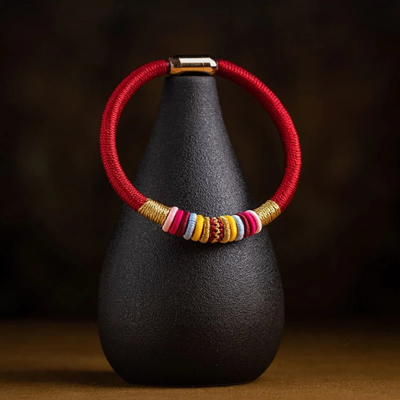 Red braided Tibetan protection bracelet with decorative knot details on display