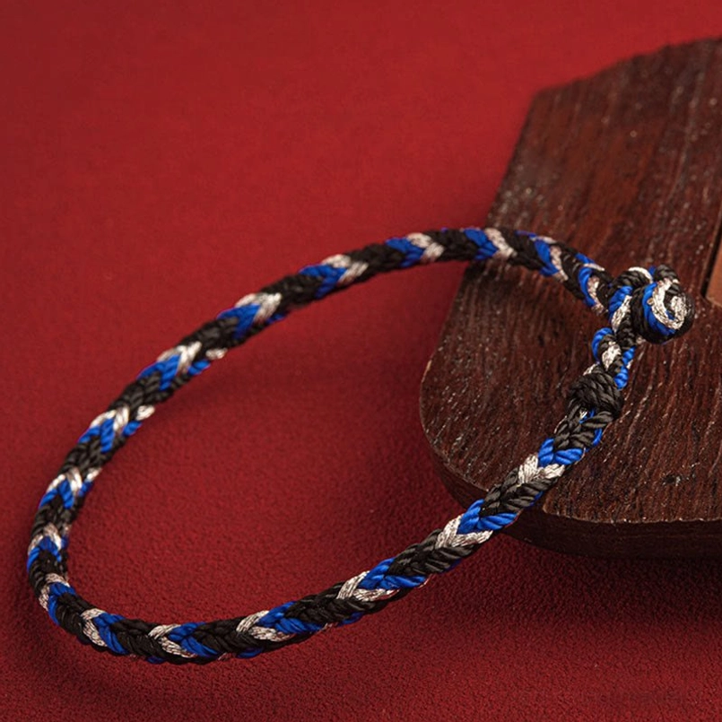 Slim tri-color braided red string bracelet with knot fastener on wooden surface