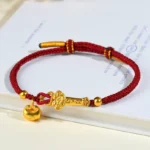 Red string Ruyi bracelet with Fu character charm and gold bell pendant on book