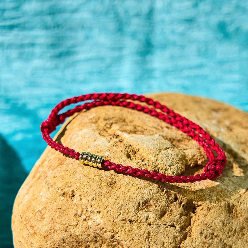 Dark red sterling silver bead bracelet overhead flat lay on yellow stone with blue backdrop