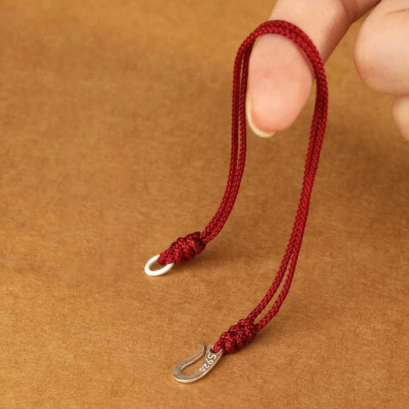 Adjustable 925 sterling silver red string bracelet with braided cord held in hand