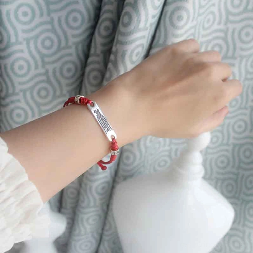 Red string lucky bracelet with sterling silver charm worn on female wrist, close-up side view