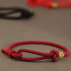 Red string sterling silver coin luck bracelet close-up side view with maroon woven rope and colorful accent bead