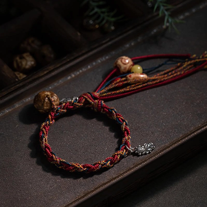 Handmade tassel bracelet featuring red-brown braided rope with silver charm and natural stone beads