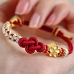 Handmade red string true love knot bracelet with gold peach blossom charm and white beaded accents close-up