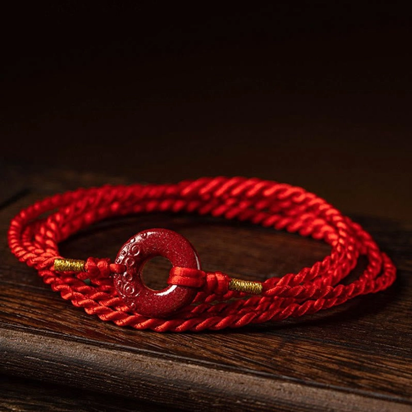 Flat lay view of red string belly chain with natural cinnabar peace buckle on wooden surface