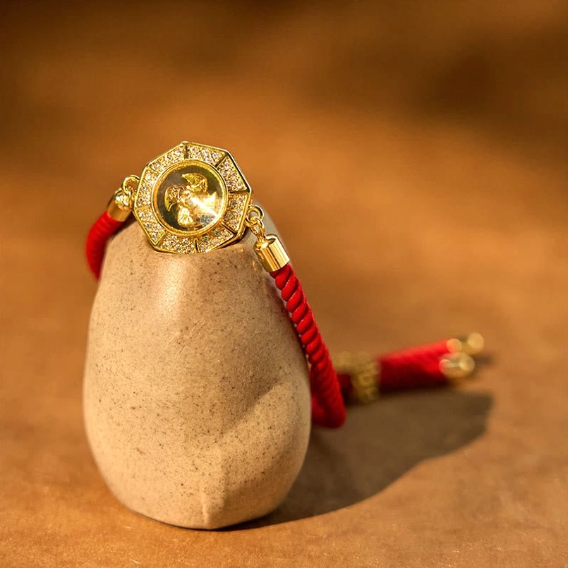 Close-up detail of rotating feng shui red string bracelet charm with polished copper hardware and woven rope