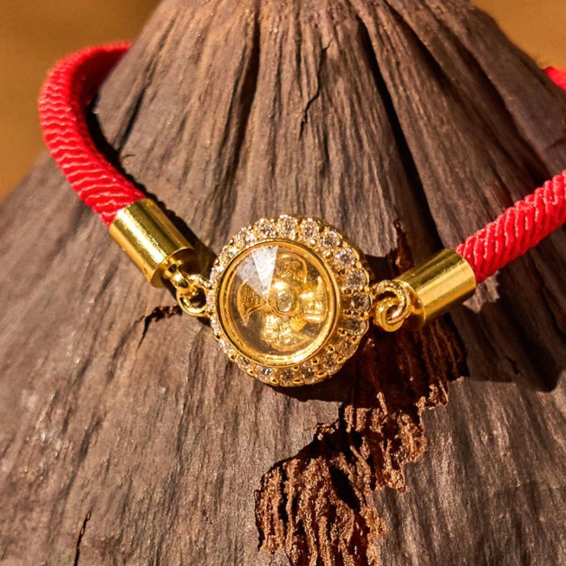 Detailed close-up of red cord feng shui bracelet charm with wide diamond halo and polished gold fittings