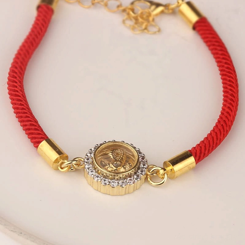 Flat lay feng shui red string protection bracelet with gold-tone windmill amulet on white ceramic background