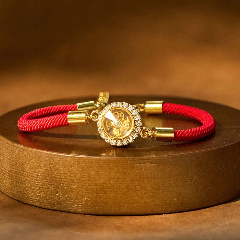 Rotating windmill red string feng shui protection bracelet with diamond-encrusted copper charm on golden display platform