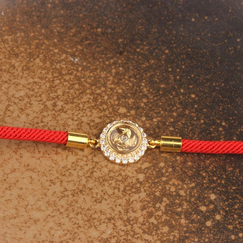 Overhead close-up of diamond-encrusted rotating windmill charm with gold cord end fittings on red string