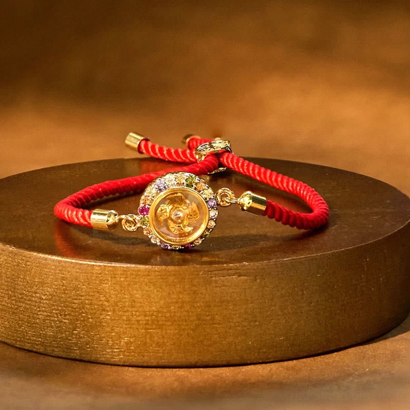 Lucky red string feng shui bracelet with rotating copper charm on wooden stand, side angle