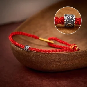 Red string Yin Yang protection bracelet with sterling silver charm on wooden background