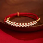 Red Tibetan peach blossom knot red string bracelet with gold accents on wooden plate