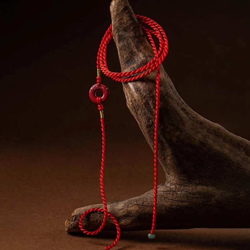 Hanging side view of red string belly chain with light green bead accent on wooden background
