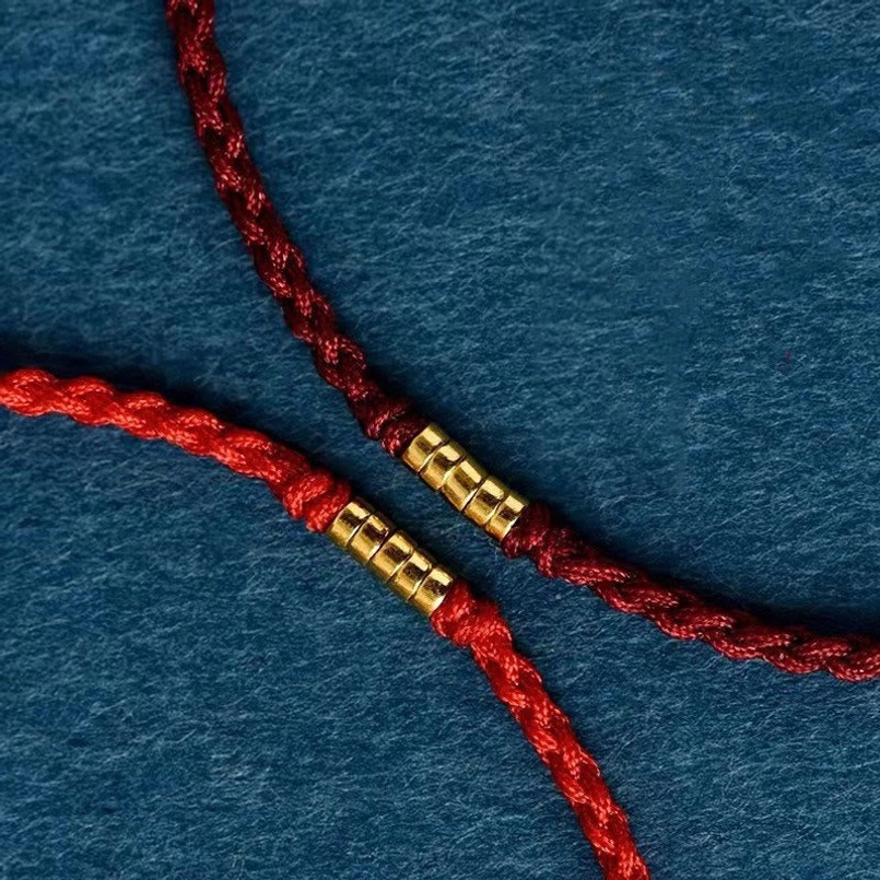 Red braided cord bracelet with cylindrical golden metal beads close-up view