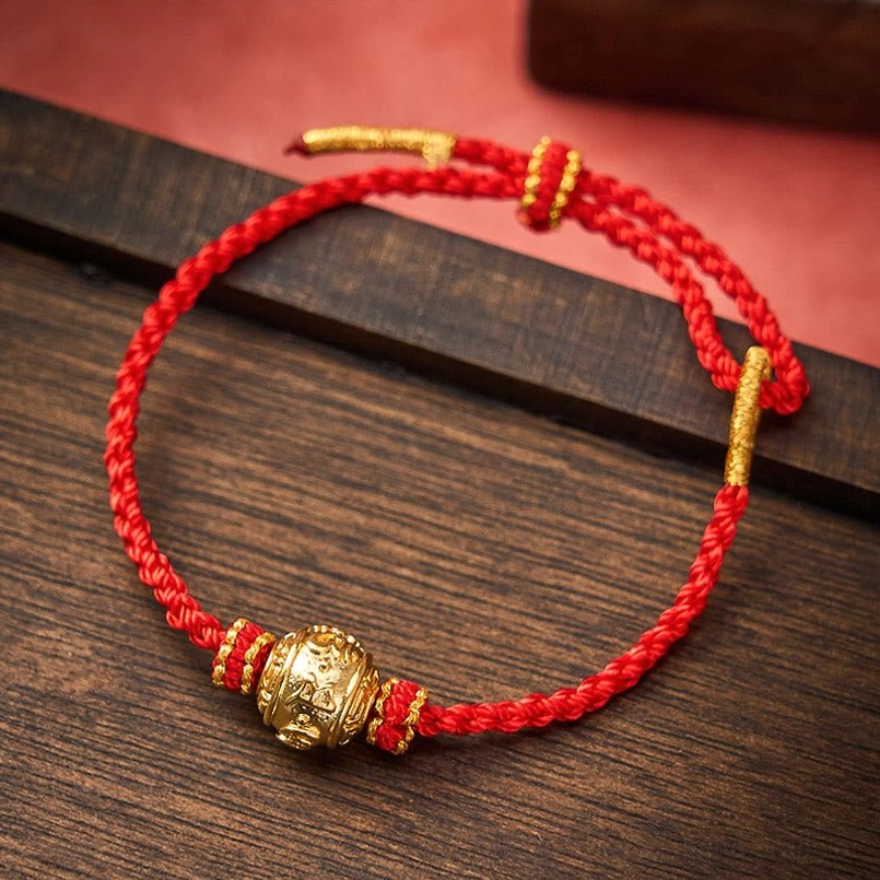 Red woven lucky bracelet with carved gold bead and red-gold knot details on dark wood