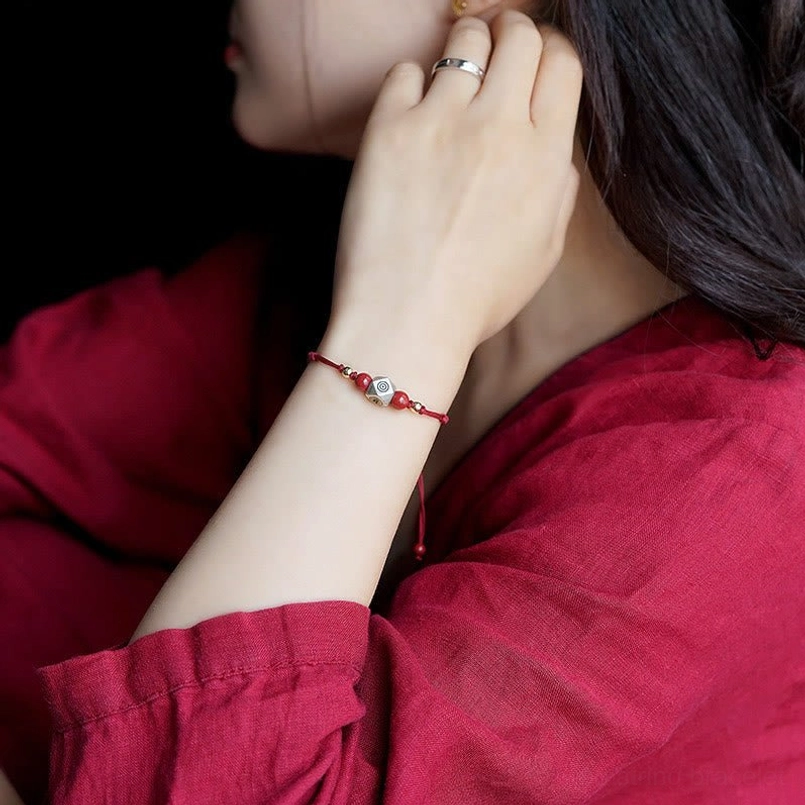 Red woven zodiac protective bracelet worn on wrist with thin decorative cord and adjustable tail