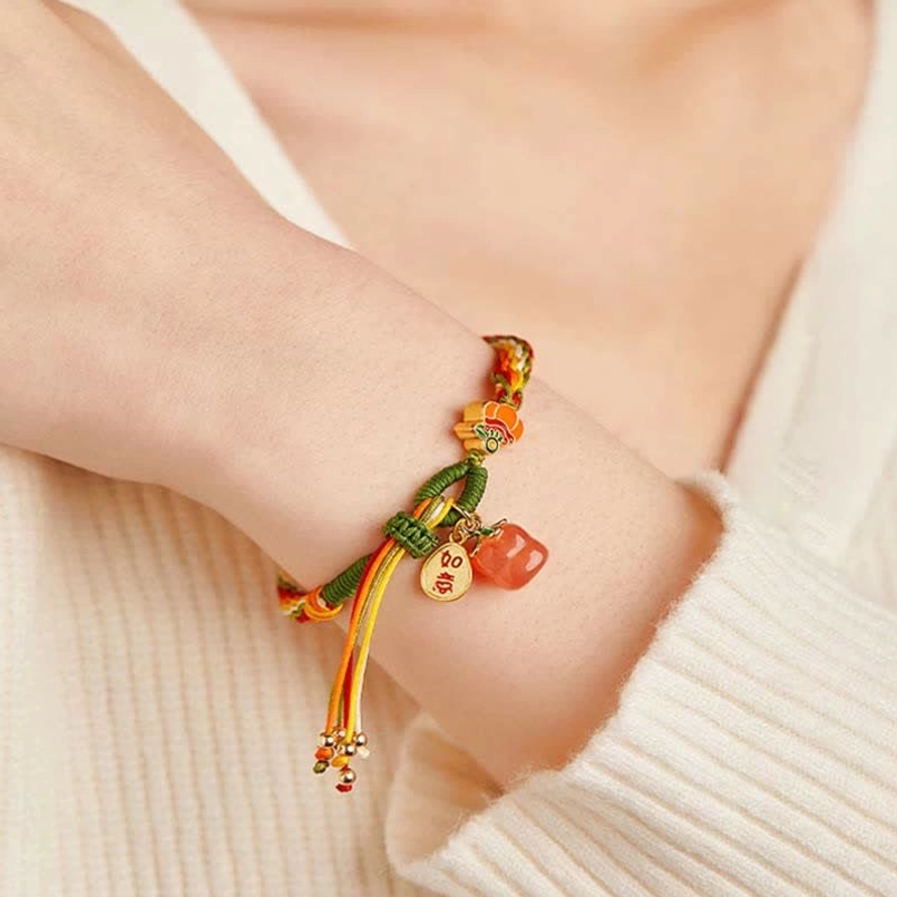 Lucky red string bracelet on wrist with persimmon agate pendant against knitted sweater