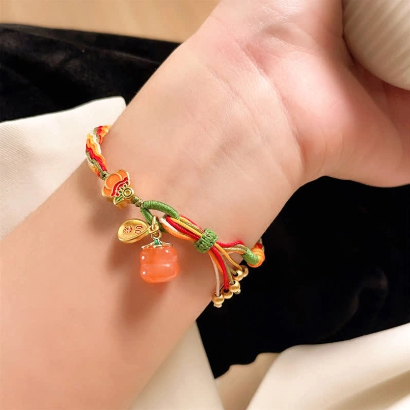 Red agate lucky bracelet with enamel flower charm and metal tags worn on wrist over dark fabric