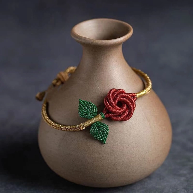 Red rose knot Tibetan peace bracelet displayed on ceramic vase with gold-brown braided cord